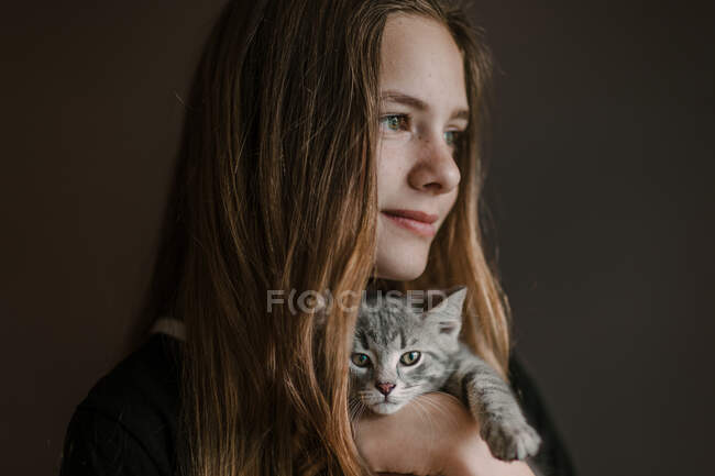 Rêveuse adolescente réfléchie tenant le chat mignon moelleux sur fond brun en studio — Photo de stock