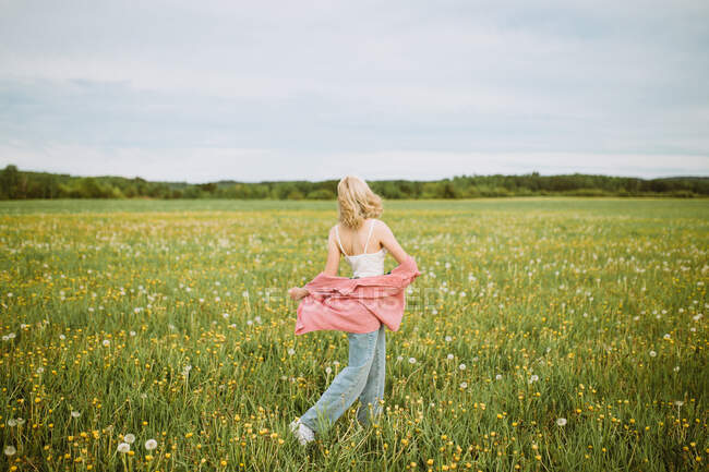 Vue latérale d'une femme anonyme marchant le long d'un champ estival en pleine floraison et jouissant de la liberté — Photo de stock