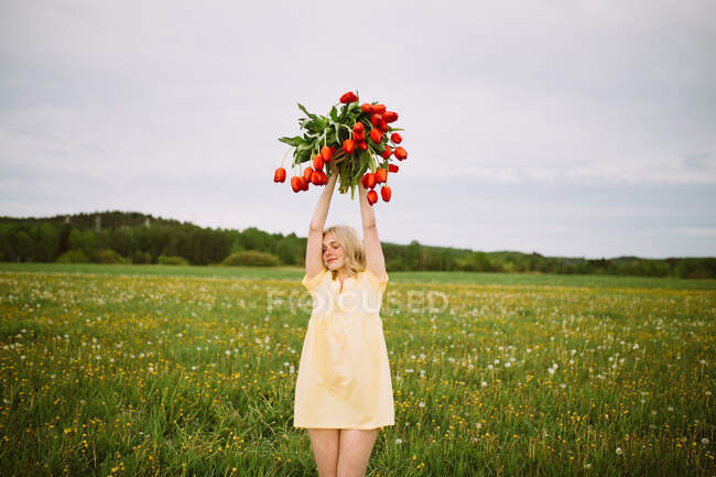 Smiling charming female with bouquet of red tulip flowers sitting in green meadow in summer — Stock Photo