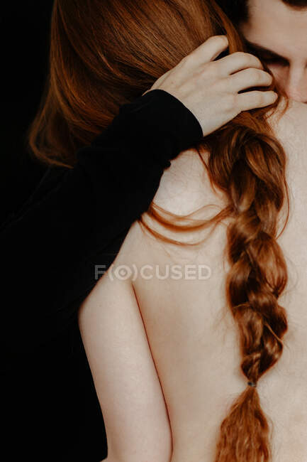 Gentle boyfriend hugging anonymous redhead shirtless girlfriend standing on black background in studio — Stock Photo