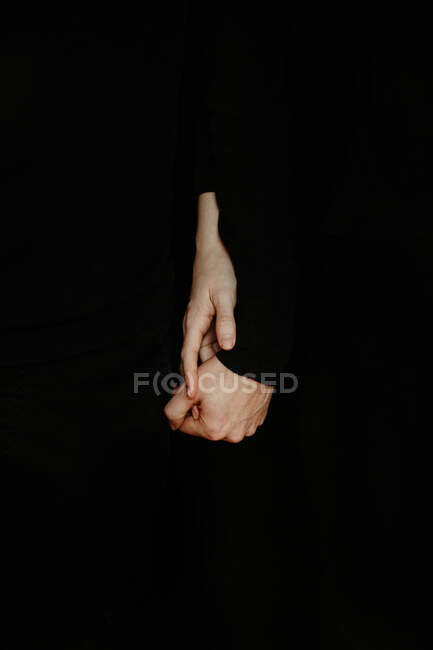 Couple amoureux des cultures méconnaissable tenant tendrement la main en studio sombre sur fond noir — Photo de stock