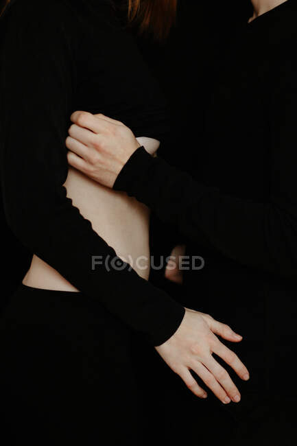 Side view of unrecognizable crop tender boyfriend touching belly of girlfriend while standing in dark studio on black background — Stock Photo