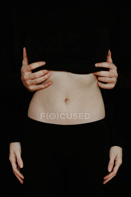 Unrecognizable crop tender boyfriend touching belly of girlfriend while standing in dark studio on black background — Stock Photo
