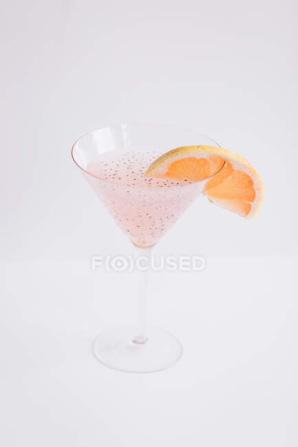 Сверху бокал свежего розового коктейля мартини с семенами чиа, украшенного ломтиком грейпфрута и помещенного на белом фоне — стоковое фото