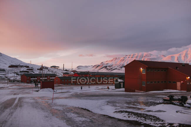 Casas residenciales rojas situadas en valle nevado en las tierras altas en invierno sobre el fondo del cielo del atardecer en Svalbard - foto de stock