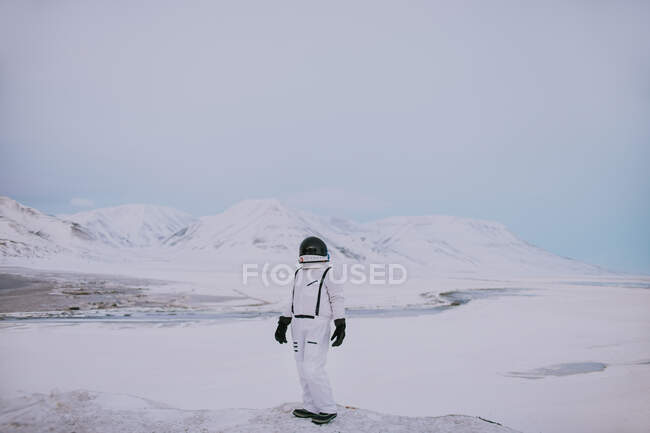 Unrecognizable cosmonaut wearing white spacesuit standing on snowy field in winter and admiring amazing landscape in Svalbard — Stock Photo