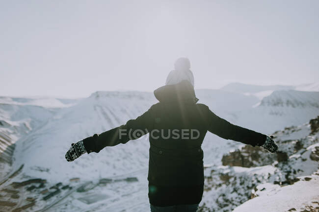 Погляд на анонімну жінку - мандрівника, що стоїть з розпростертими обіймами і насолоджується свободою в горах взимку на Свальбарді. — стокове фото