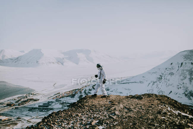Unerkennbarer Kosmonaut in weißem Raumanzug, der im Winter am Rande eines felsigen Berges steht und die atemberaubende Landschaft in Spitzbergen bewundert — Stockfoto