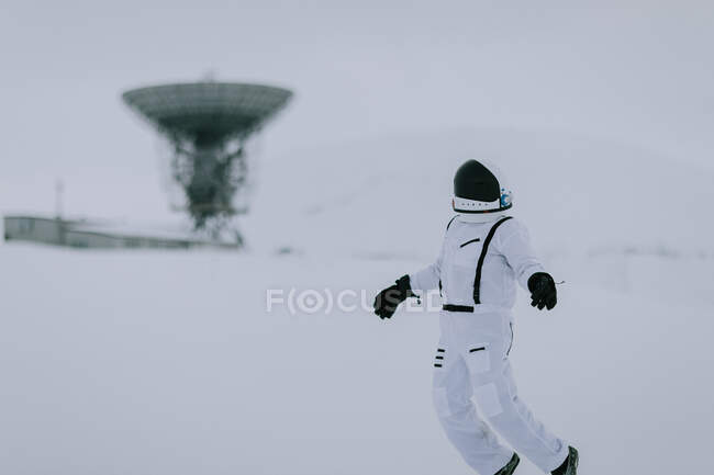 Неузнаваемый космонавт в скафандре зимой стоит в заснеженной долине на фоне огромных радиолокационных антенн на Шпицбергене — стоковое фото