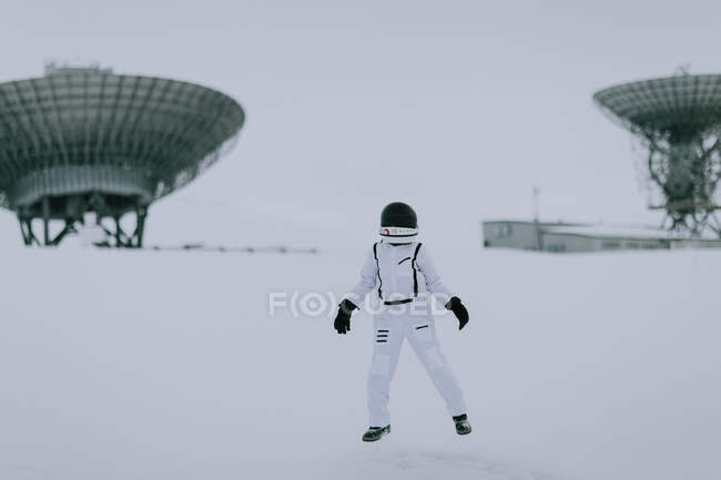 Неузнаваемый космонавт в скафандре зимой стоит в заснеженной долине на фоне огромных радиолокационных антенн на Шпицбергене — стоковое фото