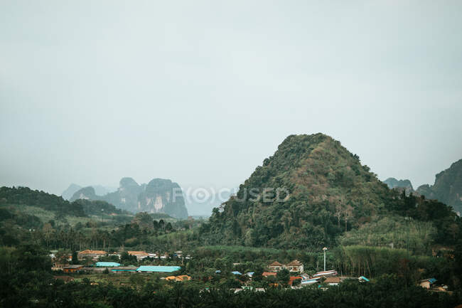 Pequena aldeia com casas residenciais rodeadas de árvores e montanhas cobertas de plantas verdes contra céu sem nuvens e formações rochosas — Fotografia de Stock