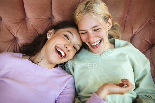 Високий кут веселих сестер-підлітків, що розслабляються на дивані та сміються, розважаючись разом у вихідні — стокове фото