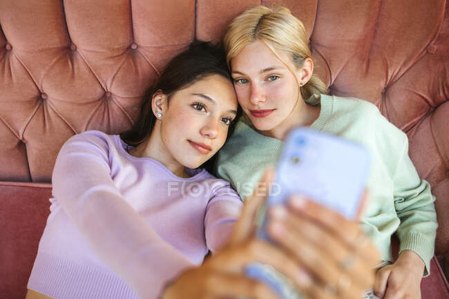 Von oben von fröhlichen jungen Schwestern, die auf dem Sofa liegen und Selbstaufnahmen mit dem Handy machen — Stockfoto