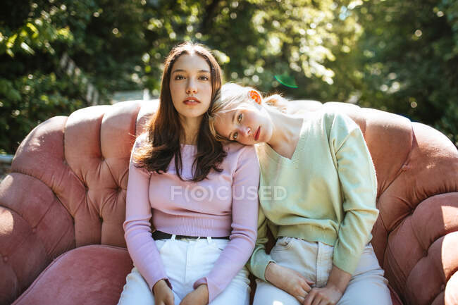 Sanfte Teenie-Schwestern sitzen an sonnigen Tagen auf einer bequemen Couch im Garten und schauen in die Kamera — Stockfoto