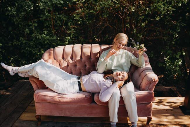 Sœurs adolescentes tranquilles se reposant ensemble sur le canapé tout en se refroidissant sur la terrasse en été par une journée ensoleillée — Photo de stock