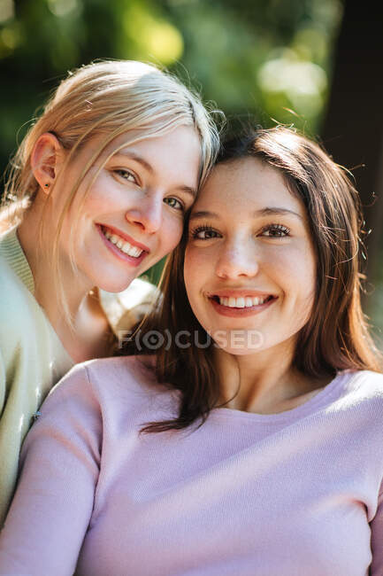 Tierna alegre adolescente hermanas mirando a la cámara en el soleado día de verano en el jardín verde - foto de stock