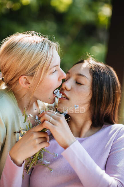 Deliciosas hermanas adolescentes con ramita de hierba en los dientes abrazando y divirtiéndose en el día soleado en el jardín - foto de stock