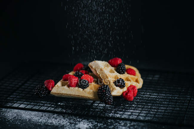 Süße Waffeln serviert mit frischen Beeren und Zuckerpulver auf schwarzem Hintergrund — Stockfoto