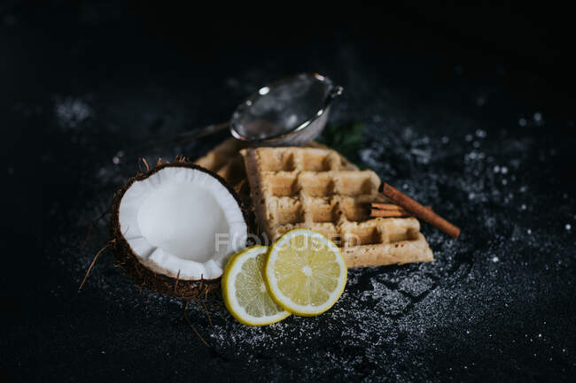 Alto ángulo de sabrosos gofres veganos servidos en mesa negra con rodajas de coco y limón - foto de stock