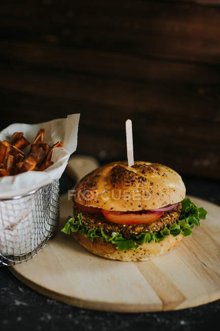 Appetizing vegan burger with vegetables served on wooden board with sweet potato fries in metal basket — Stock Photo