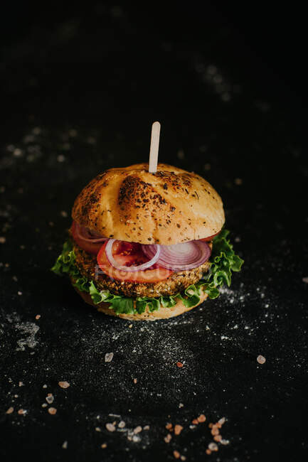 Hambúrguer vegan saboroso com legumes maduros frescos servidos em fundo preto em estúdio — Fotografia de Stock