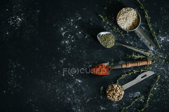Vue du dessus des cuillères avec du paprika et des herbes sèches placées sur une table noire avec de l'avoine et des graines de tournesol — Photo de stock