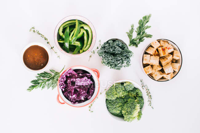 Вид зверху на свіжі овочі та смажене тофу, розташоване на білому столі з соусом, приготованим для вегетаріанського салату — стокове фото