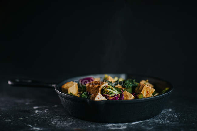 Vegetarian salad with fried tofu and vegetables served on black background — Stock Photo