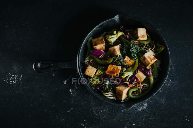 Сверху вегетарианский салат с жареным тофу и овощами подается на черном фоне — стоковое фото