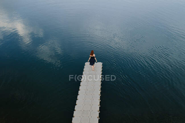 From above remote view of female standing on edge of quay near calm lake — Stock Photo
