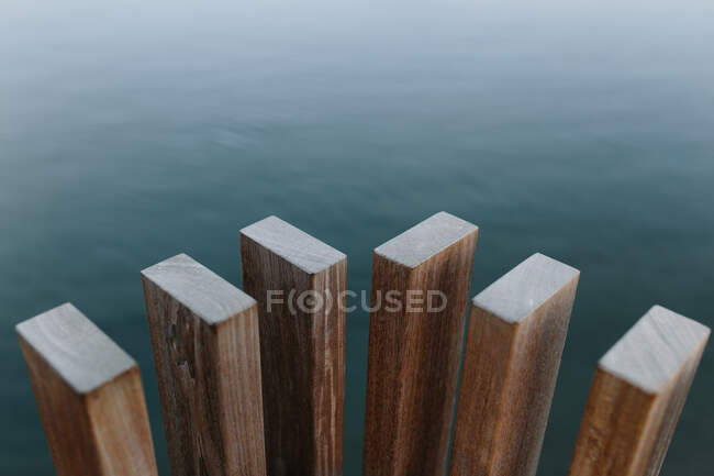 Alto ángulo de vigas de madera modernas colocadas cerca del estanque con agua tranquila durante el día - foto de stock