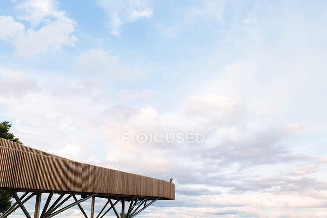 Vista remota de la persona de pie en el mirador de madera en el fondo del increíble cielo nublado puesta de sol - foto de stock
