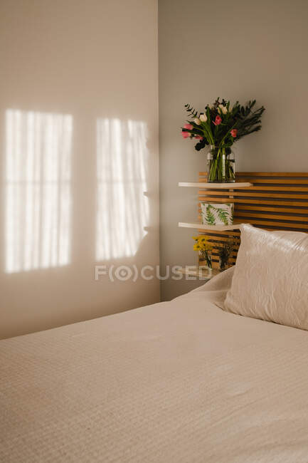 Incrível buquê de tulipas e decoração perto da cama em um quarto brilhante e ensolarado — Fotografia de Stock