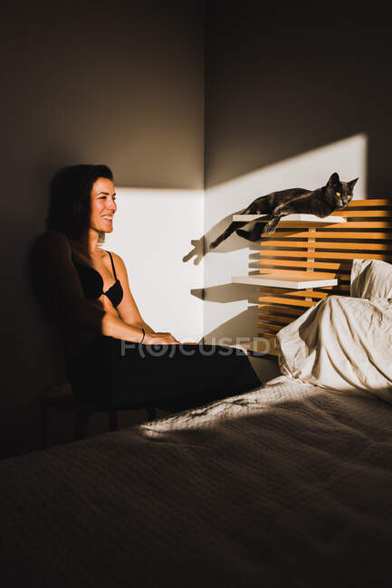 Без сорочки жінка біля милого кота в полиці спальні крупним планом ліжко зі світлом, що потрапляє в кімнату — стокове фото