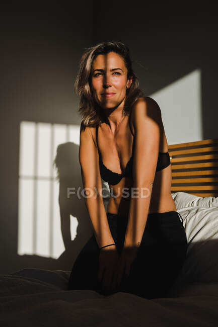 Tournage d'une jolie femme sensuelle souriant entre la lumière et les ombres dans la lingerie sur le lit regardant loin — Photo de stock