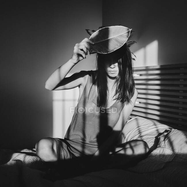 Scatto in bianco e nero di una bella donna sensuale che gioca tra luce e ombra in lingerie coprendo con foglia di pianta — Foto stock