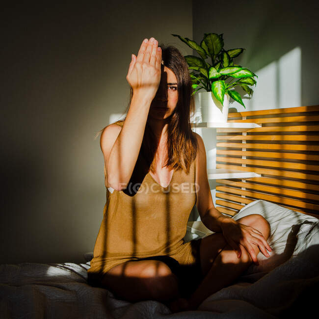 Снимок чувственной симпатичной женщины, играющей между светом и тенью, закрывающей рукой глаз — стоковое фото