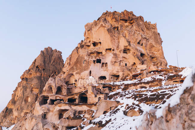 Low angle of aged castle carved in rock and covered with white snow against cloudless sky on street of Uchisar settlement in Cappadocia, Turkey — Stock Photo