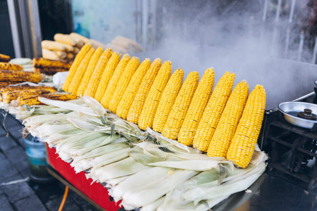 Свежий сырой и жареный кукурузные початки устроены на стойле уличной закусочной против парового горшка в городе в Турции — стоковое фото