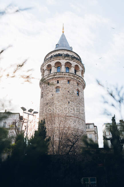Desde abajo envejecido Torre Galata situado cerca de edificio residencial contra el cielo nublado en la calle de Estambul, Turquía - foto de stock
