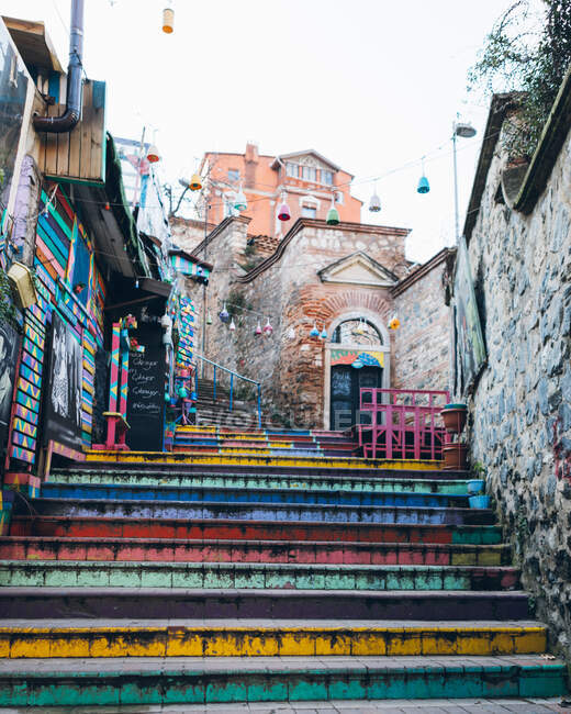Shabby escaleras multicolores bajo guirnaldas cerca de edificios de piedra envejecidos en la calle de la ciudad en Turquía - foto de stock