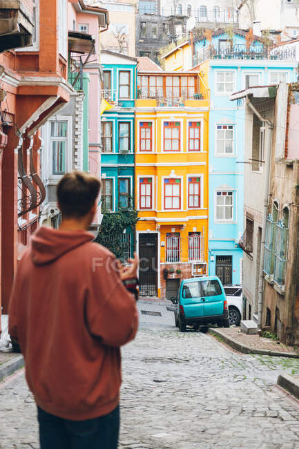 На задньому плані нерозпізнаний молодий чоловік з фотокамерою стоїть на брукованій дорозі біля яскравих будинків і синя машина на вулицях міста в Туреччині. — стокове фото