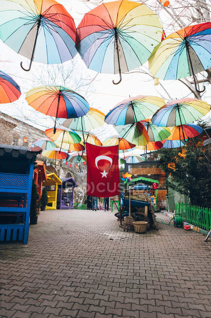 Muchos paraguas multicolores y bandera nacional de Turquía colgando sobre refugios de colores en la calle pavimentada durante el festival - foto de stock