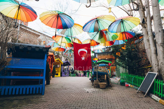 Many multicolored umbrellas and national flag of Turkey hanging over colorful shelters on paved street during festival — Stock Photo