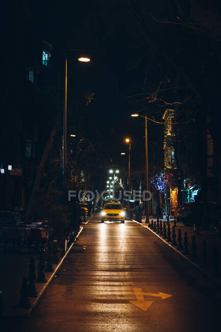 Cabina amarilla con faros brillantes que conducen por la calle de la ciudad pavimentada por la noche en Turquía - foto de stock