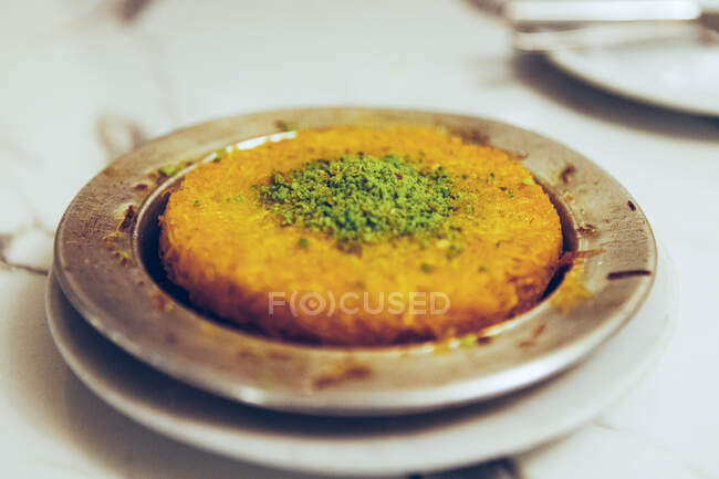 From above yummy orange pastry Kunefe with cheese with green pistachio powder and syrup on plates on table in Turkish restaurant — Stock Photo