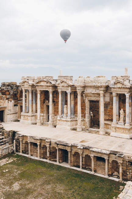 From below gray air balloon racing in cloudy sky over abandoned ancient palace with amazing architecture including columns and statues in overcast weather in Turkey — Stock Photo