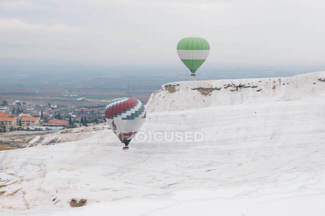 Bunte Luftballons fliegen bei bewölktem Wetter in der Türkei über mineralische Felsformation gegen neblige Stadt — Stockfoto