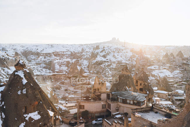 Desde arriba famoso asentamiento con antiguos edificios de piedra sabiendo como casas de hadas en el valle contra la colina nevada en invierno día soleado en Turquía - foto de stock