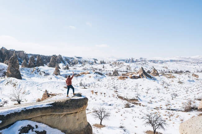 Dall'alto corpo pieno irriconoscibile turista uomo in piedi sulla pietra e ammirare incredibili viste panoramiche innevate sul cielo blu senza nuvole su terreni montagnosi innevati sulla giornata invernale soleggiata in Cappadocia, Turchia — Foto stock